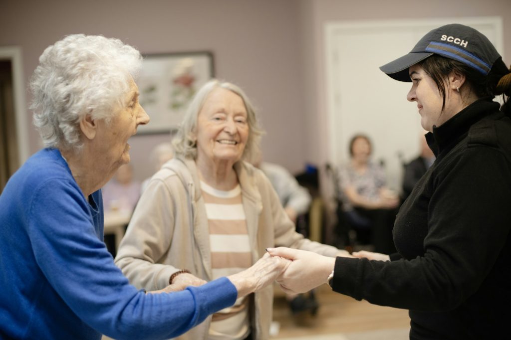A care home staff member holding hands with two residents