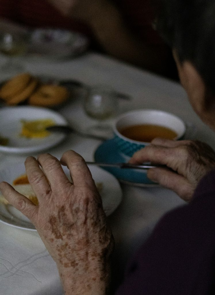 Older person’s hands holding a cup of tea at a table